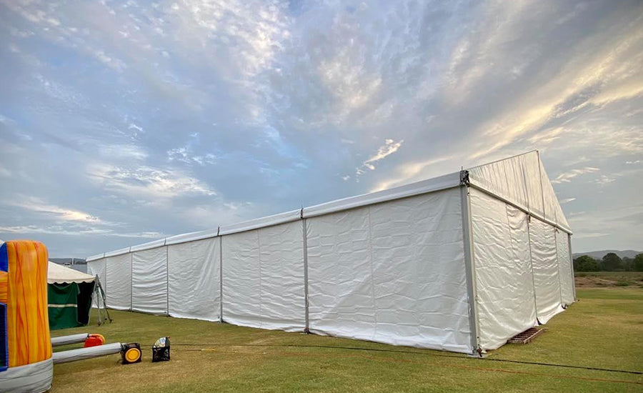 A large white event crest tent set up on a grassy field under a cloudy sky.